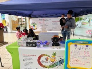 A fruit ice stand set up in a mall. People, including a child, are near the stand.