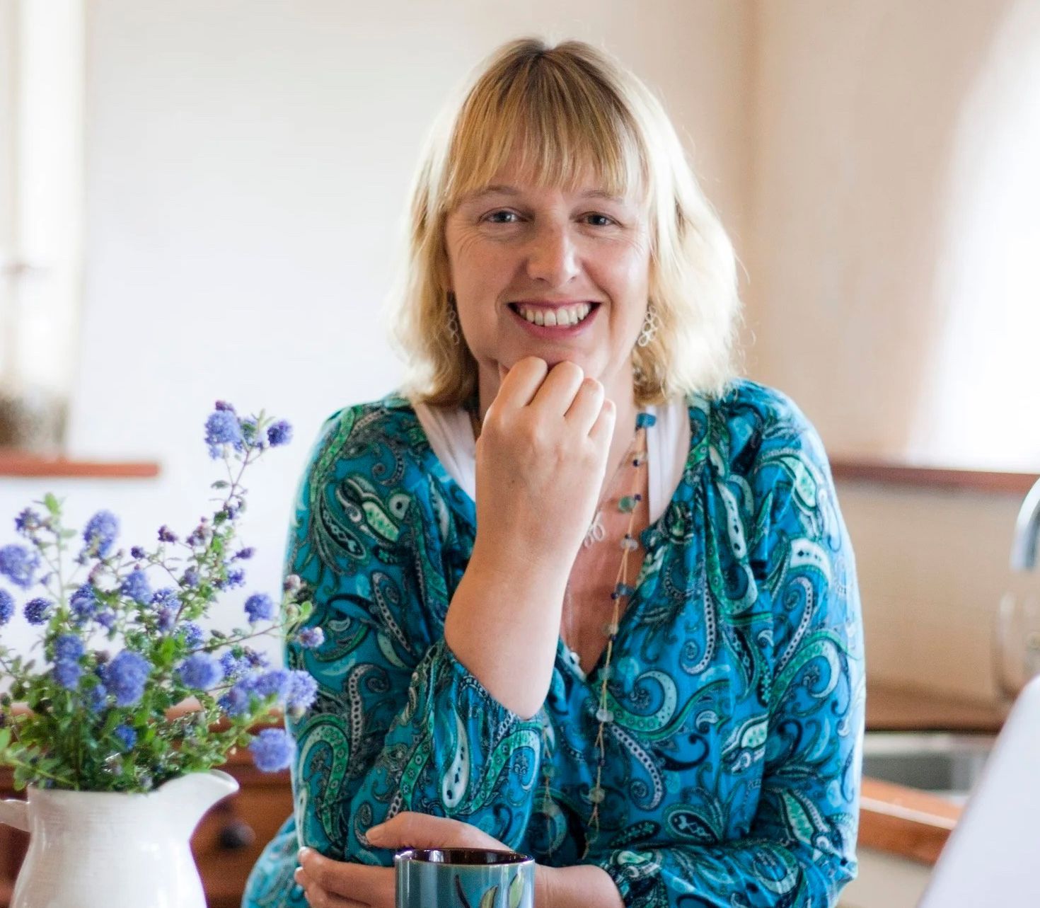 A woman in a white shirt is smiling in front of a tree.