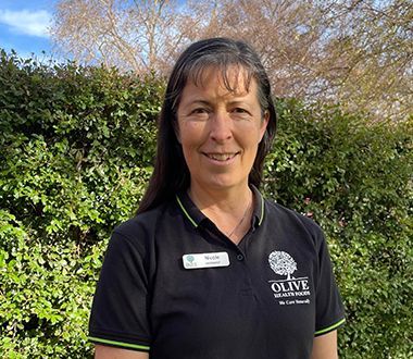 A woman in a black shirt is standing in front of a hedge.