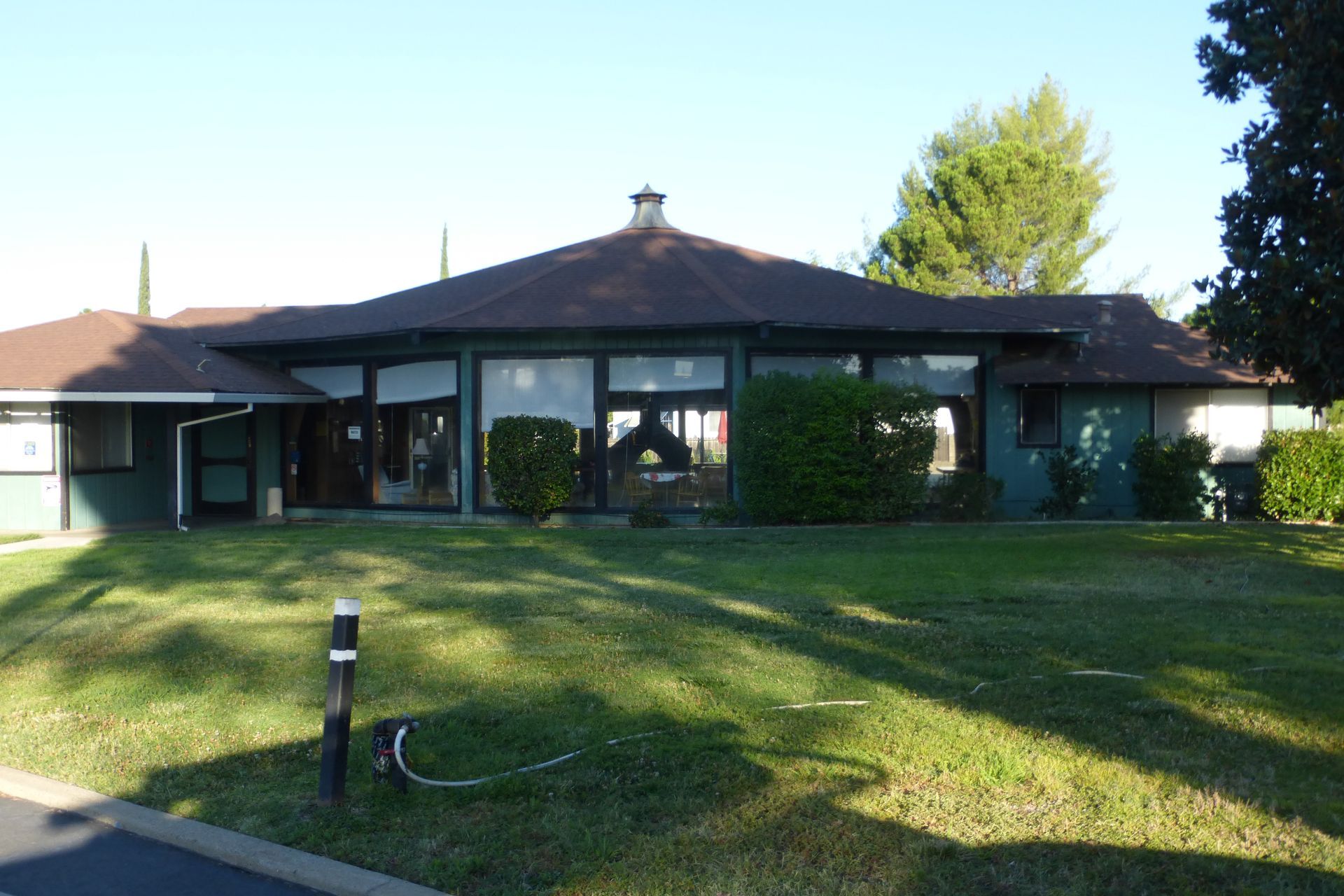 A low, teal-colored building with large windows and a circular, brown roof, set on a green lawn.
