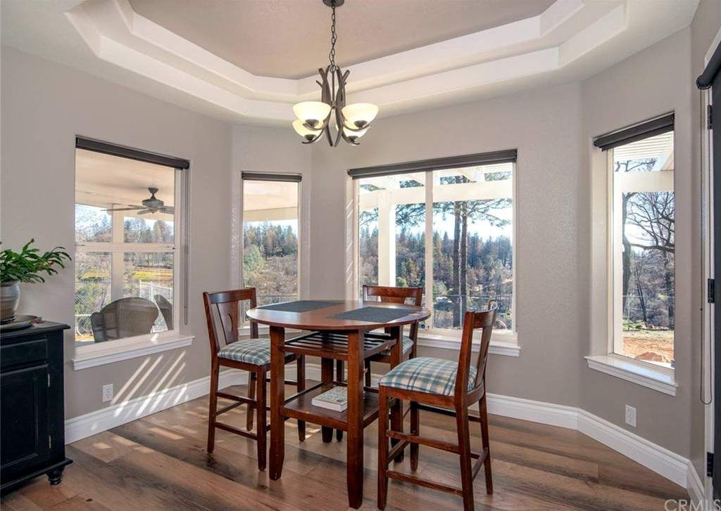 Dining room with round table, four chairs, multiple windows, chandelier, wood floor, and gray walls.