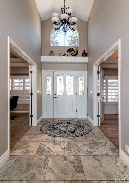 Entryway with white door, arched window, chandelier, and round rug on stone tile floor.