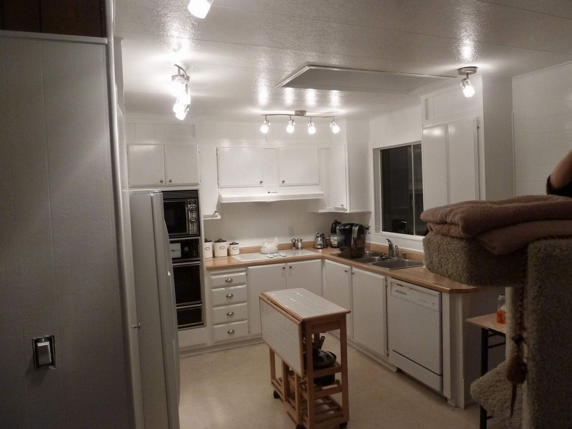 White kitchen with appliances, cabinets, and a fold-out table. Fluorescent lights.