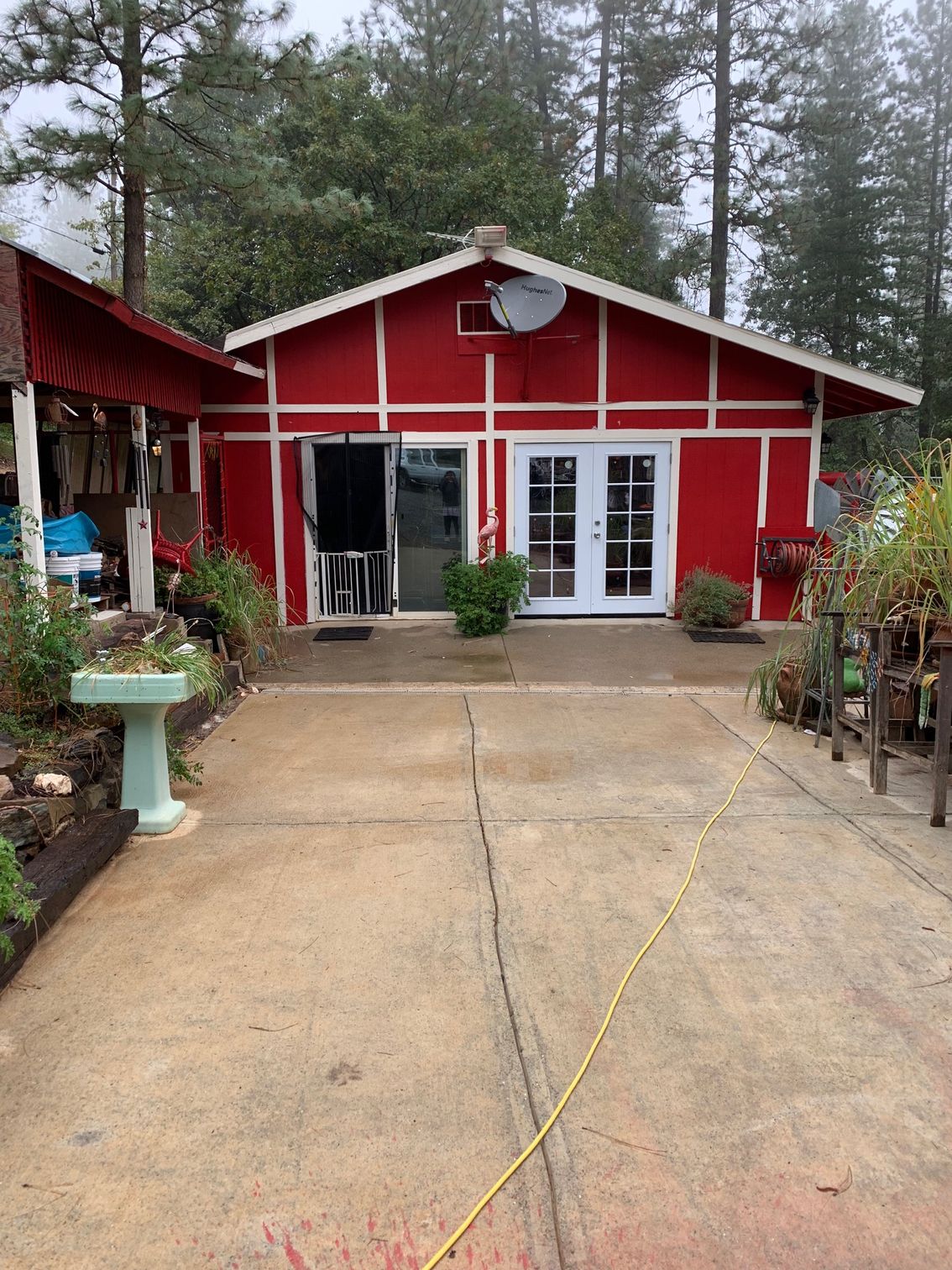 Red building with white trim and double doors. Concrete driveway, plants, and trees are in the setting.