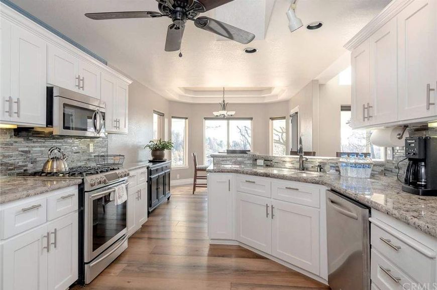 White kitchen with stainless steel appliances, pendant lights, and a stone backsplash.