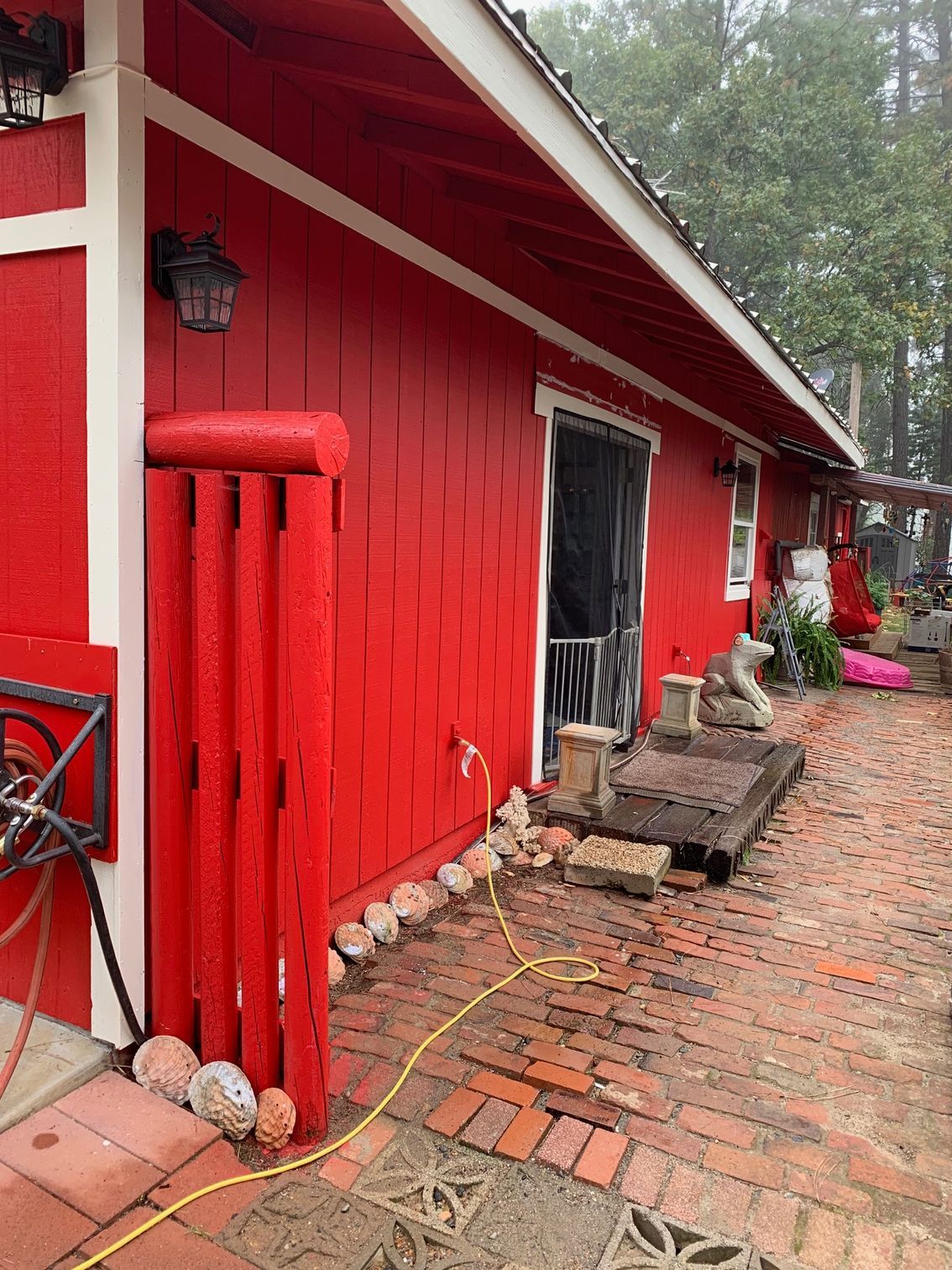 Red building with white trim, brick patio, and sliding door. A water hose and decorative stones are visible.