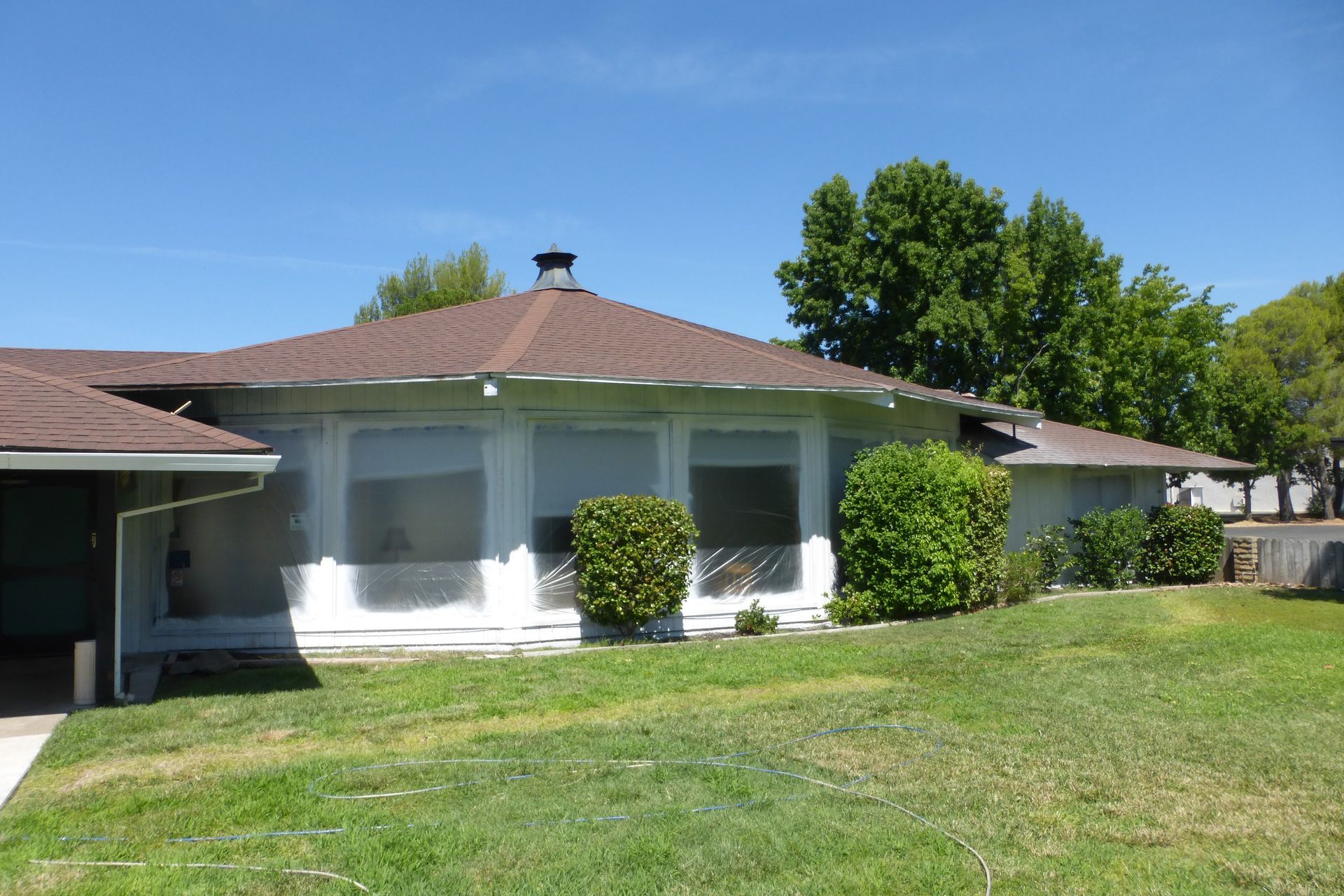 Low-angle view of a one-story house with a brown roof and a green lawn on a sunny day.