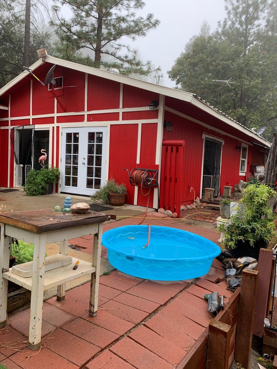 Red barn-style building with white trim, patio, blue kiddie pool, and outdoor table on a cloudy day.