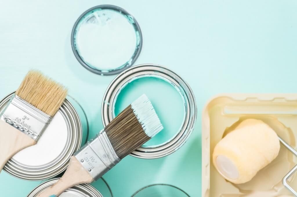 Open paint cans and brushes with light blue paint; paint roller in a tray.