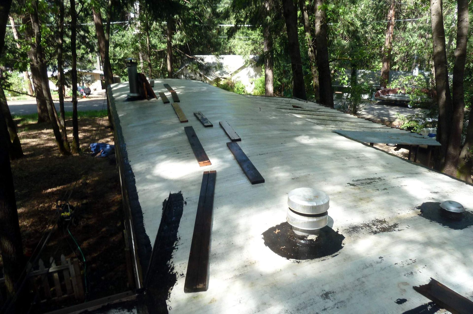 RV roof with black sealant and wood strips. Trees and buildings in background.