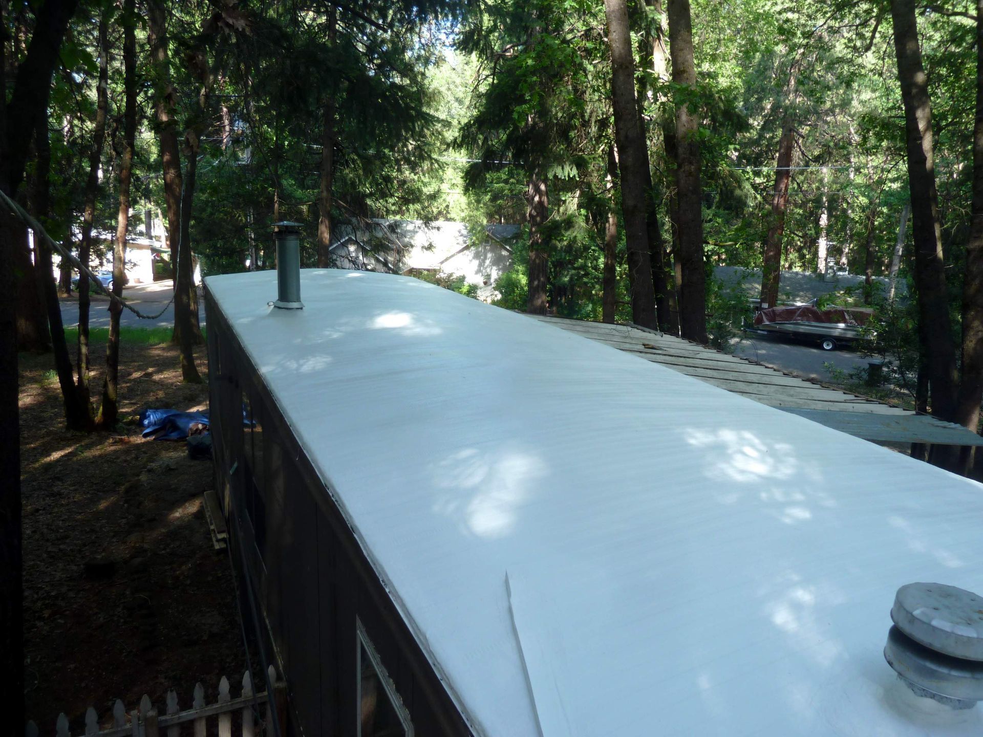 White-painted roof of a mobile home surrounded by trees in a wooded setting.