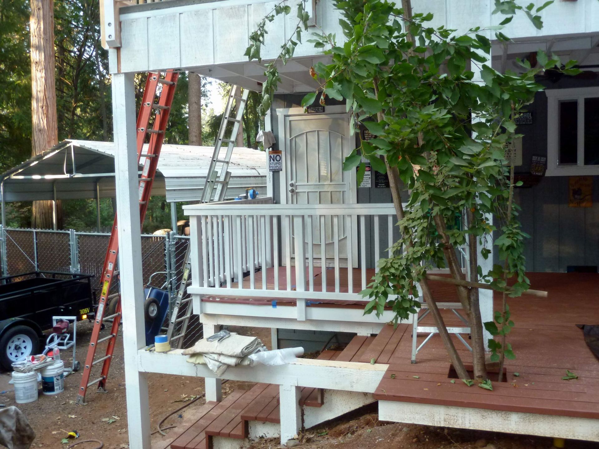 Porch with white railings being painted; ladder propped against it; tree to the right.