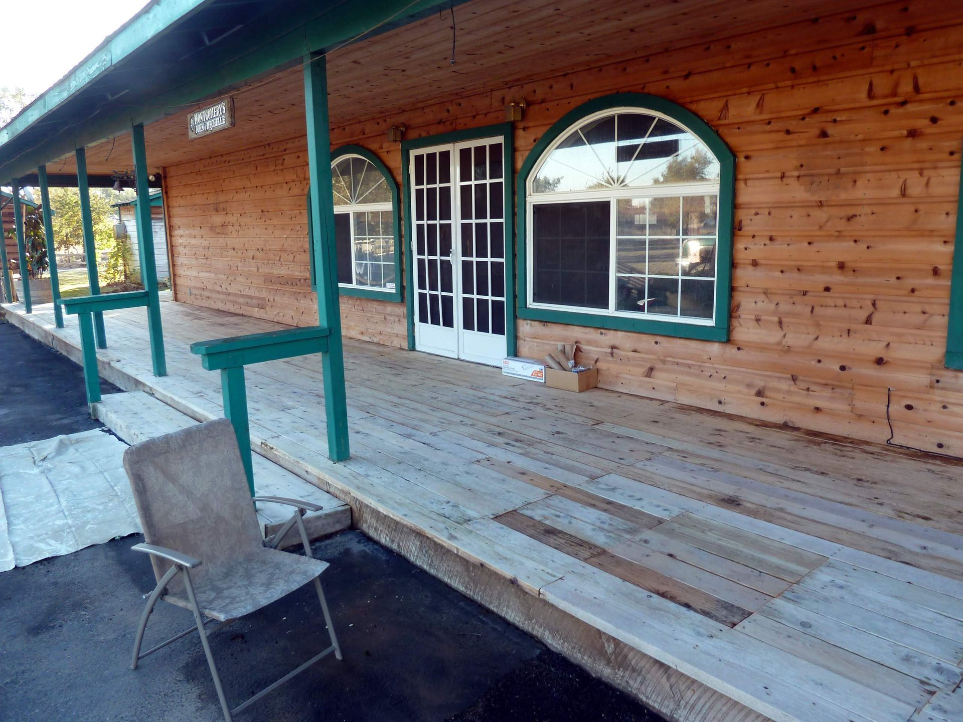 Wooden building with green trim, arched windows, and a porch. An empty chair sits on the porch.