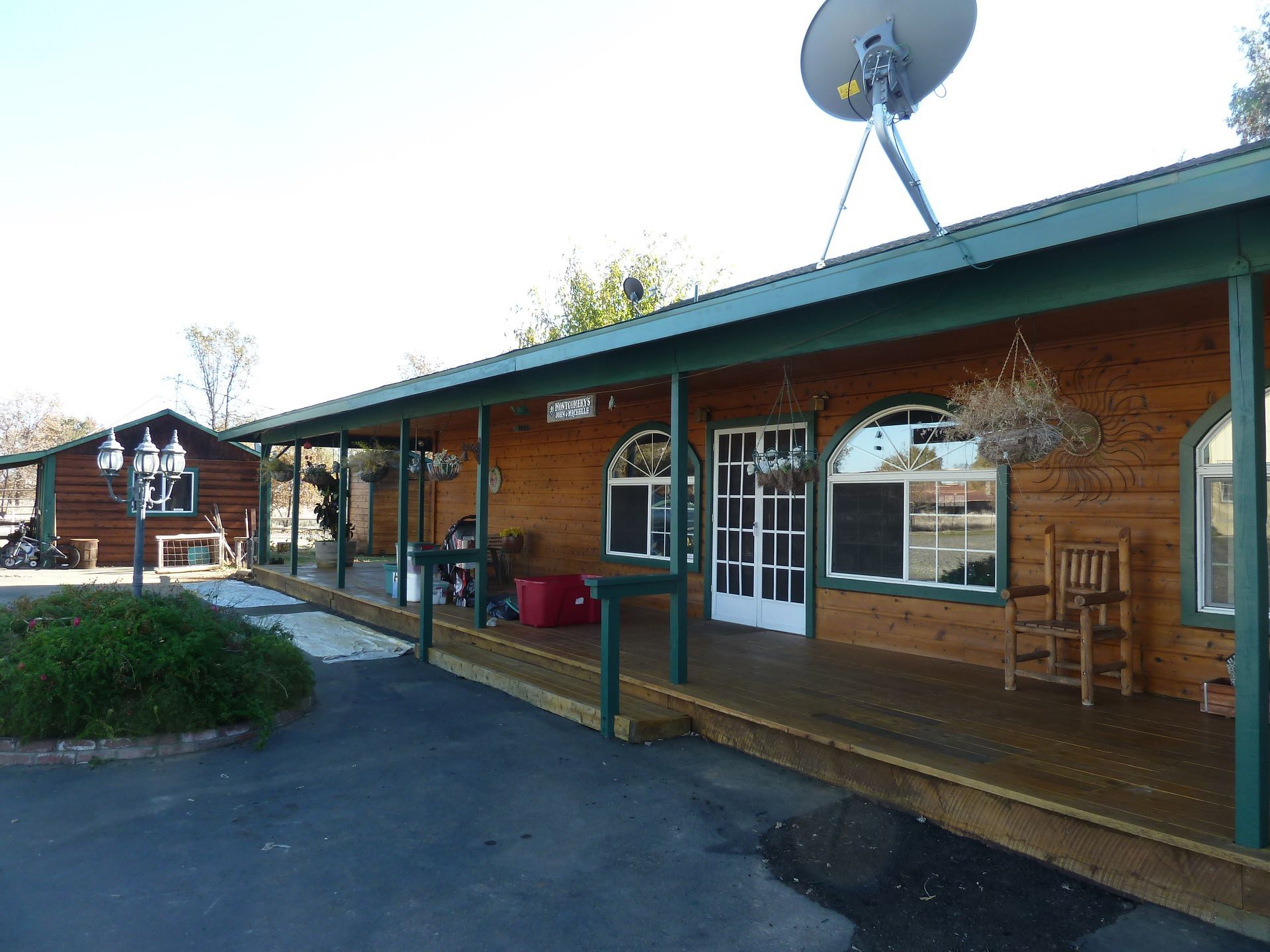 Log cabin with long porch, satellite dish, and hanging basket, set in a sunny location.