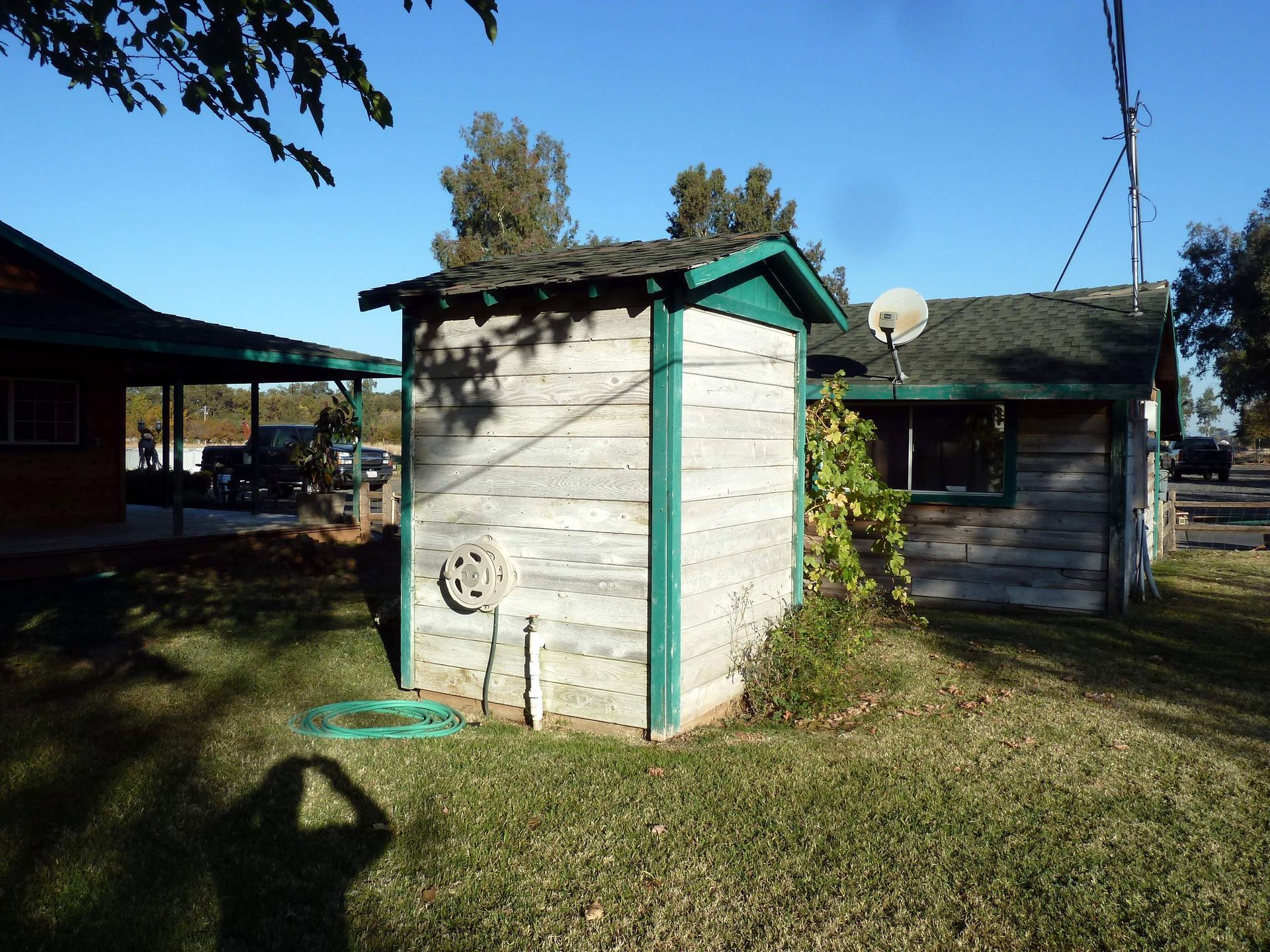 Old wooden shed with green trim and a small building next to it, under a blue sky.
