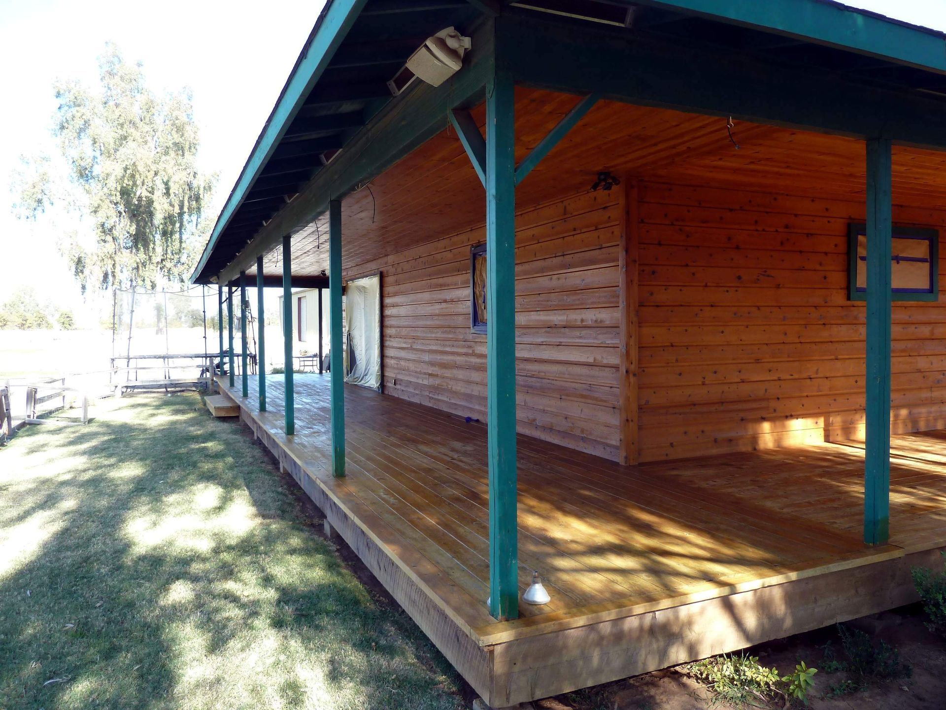 Wooden cabin with green trim and a covered porch on a sunny day.