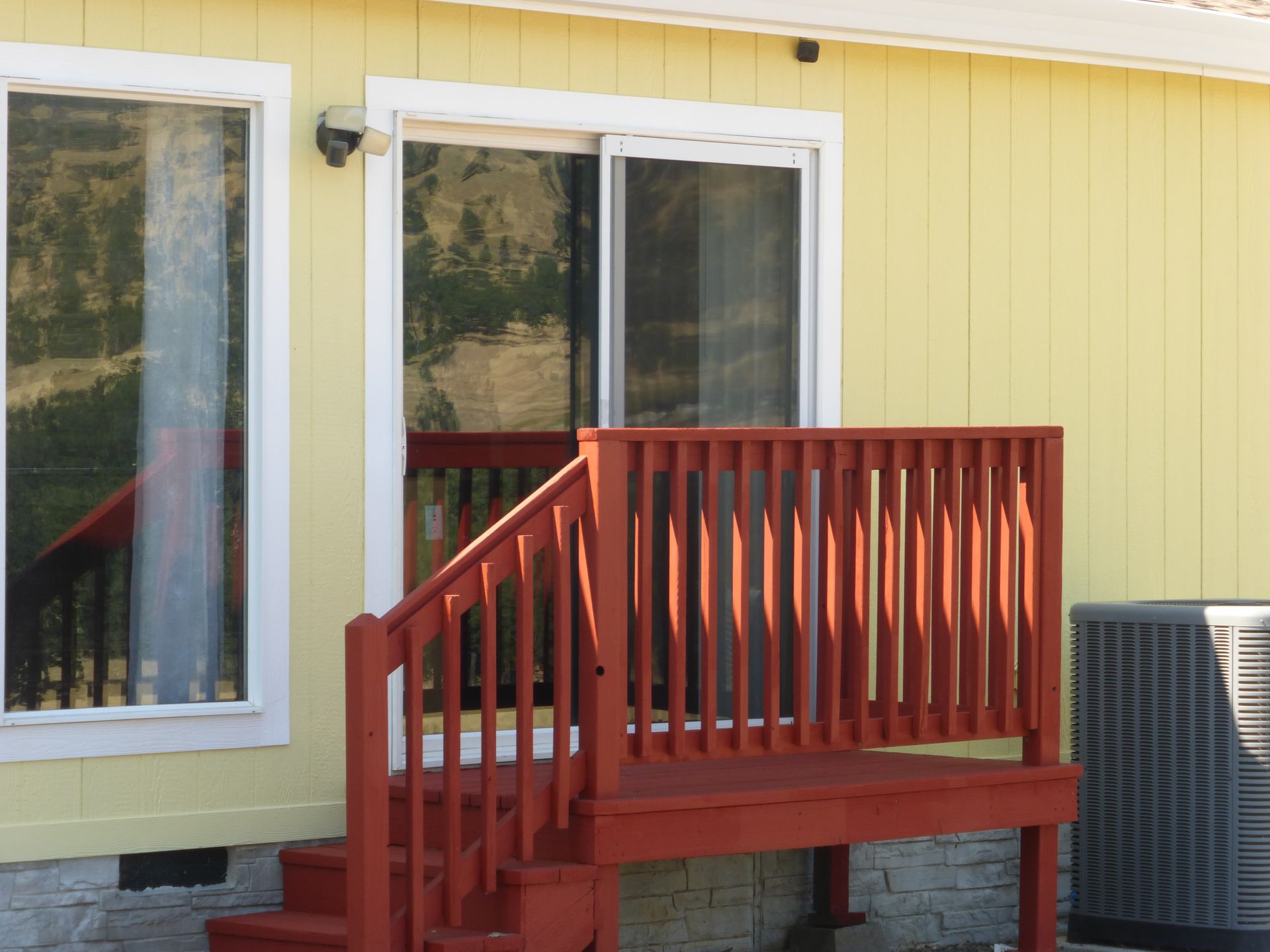 Red wooden deck with steps leading to a sliding glass door and windows on a yellow house.