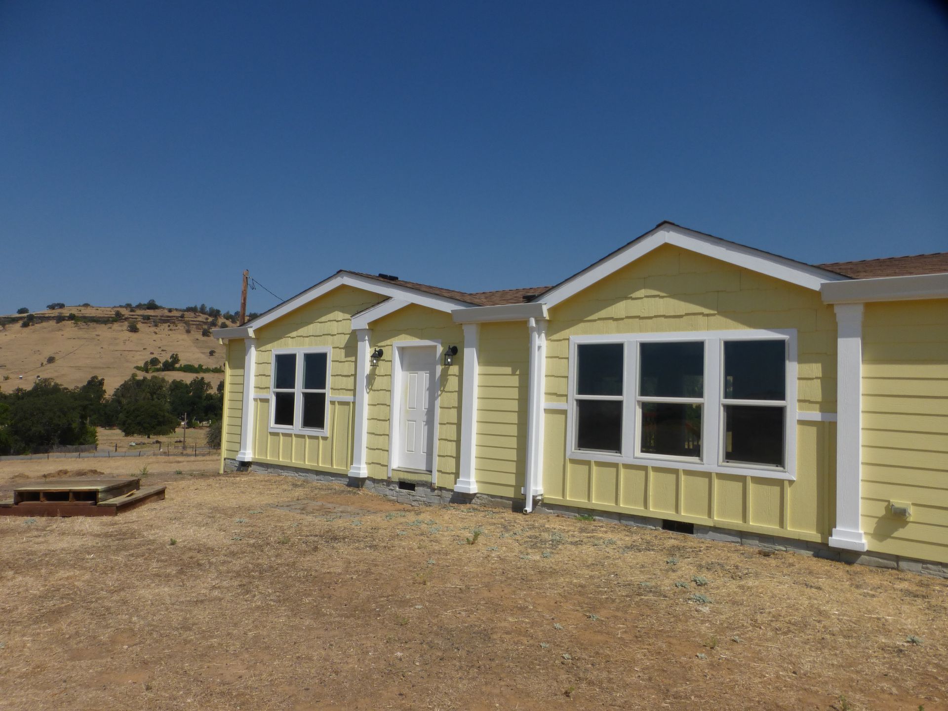 Yellow house with white trim against a blue sky, set on dry, brown land.