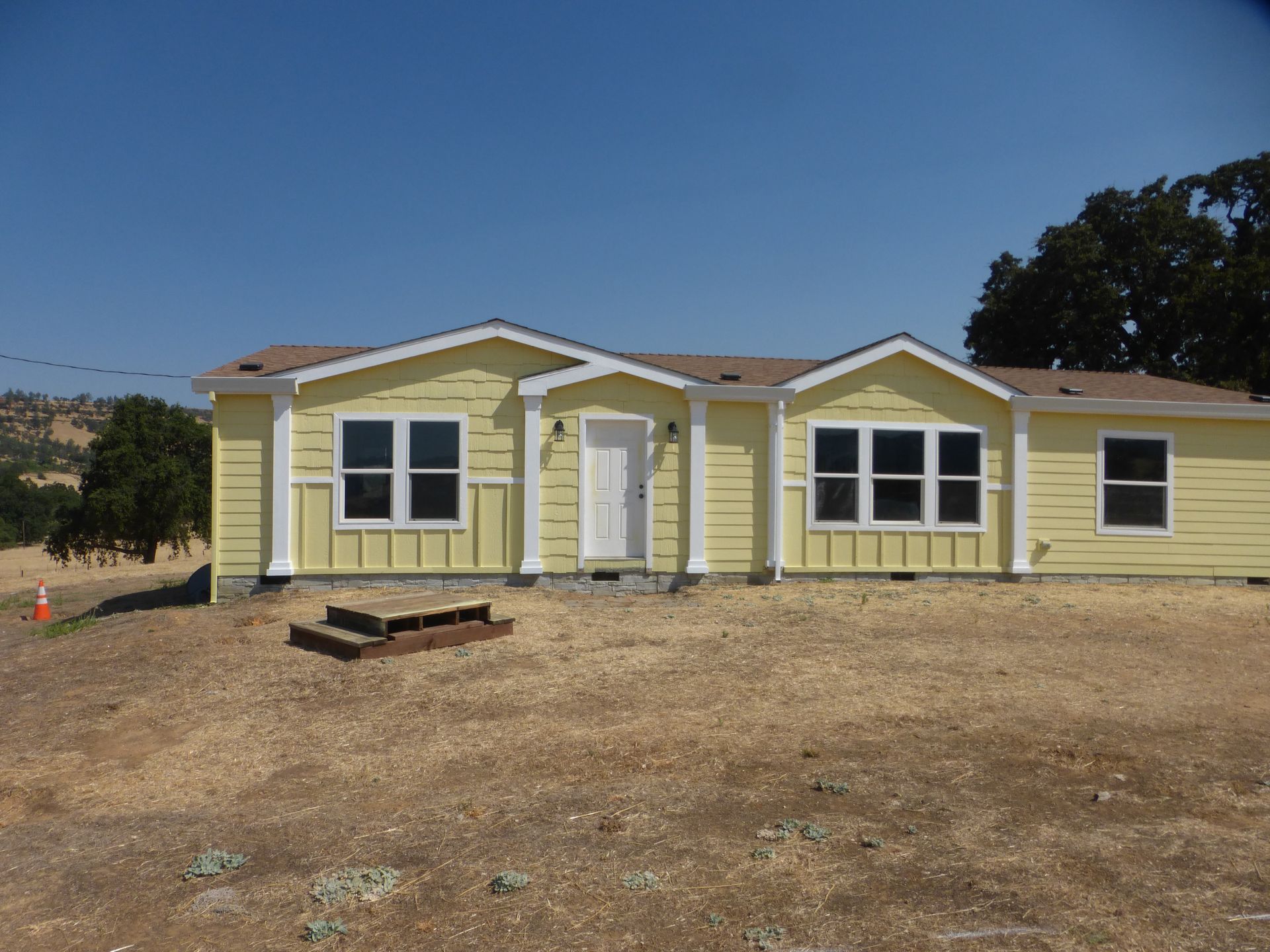 Yellow house with white trim and windows in a dry, grassy field under a blue sky.