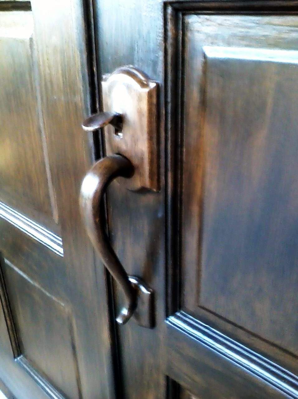 Bronze door handle on a dark brown wooden door.