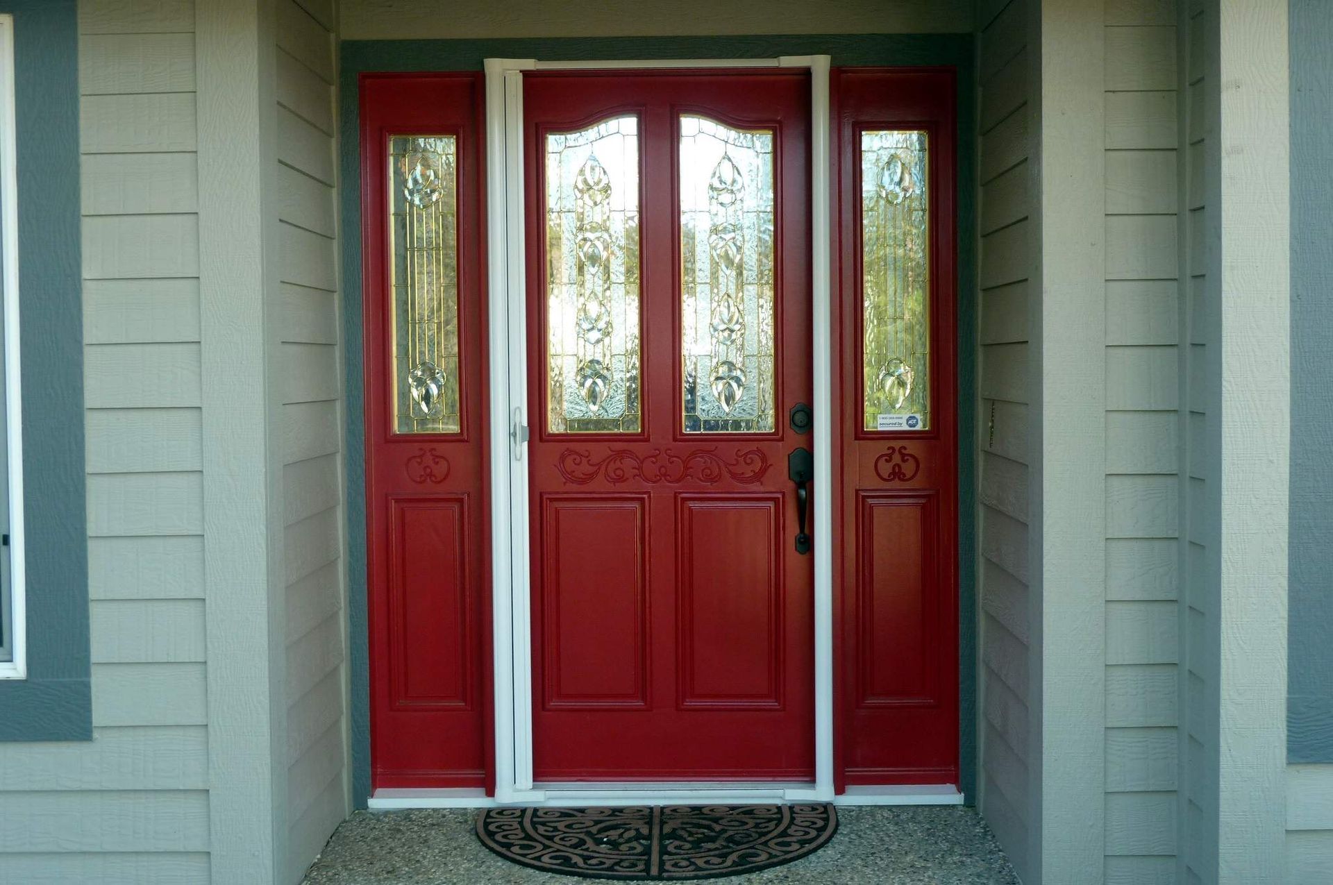 Red front door with glass panels and side lights, white trim, and a black doormat.