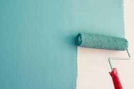 Paint roller applying turquoise paint to a white wall.