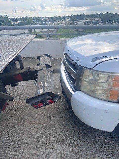 A silver car being towed by a blue tow truck on asphalt.