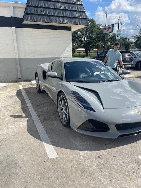 A gray Lotus sports car parked in a parking space, a man walks beside it.