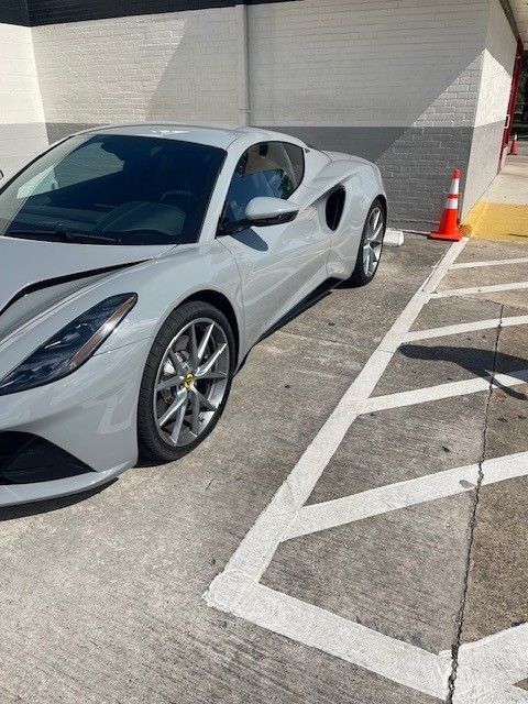 Gray Lotus sports car parked in a marked parking space with a traffic cone beside it.