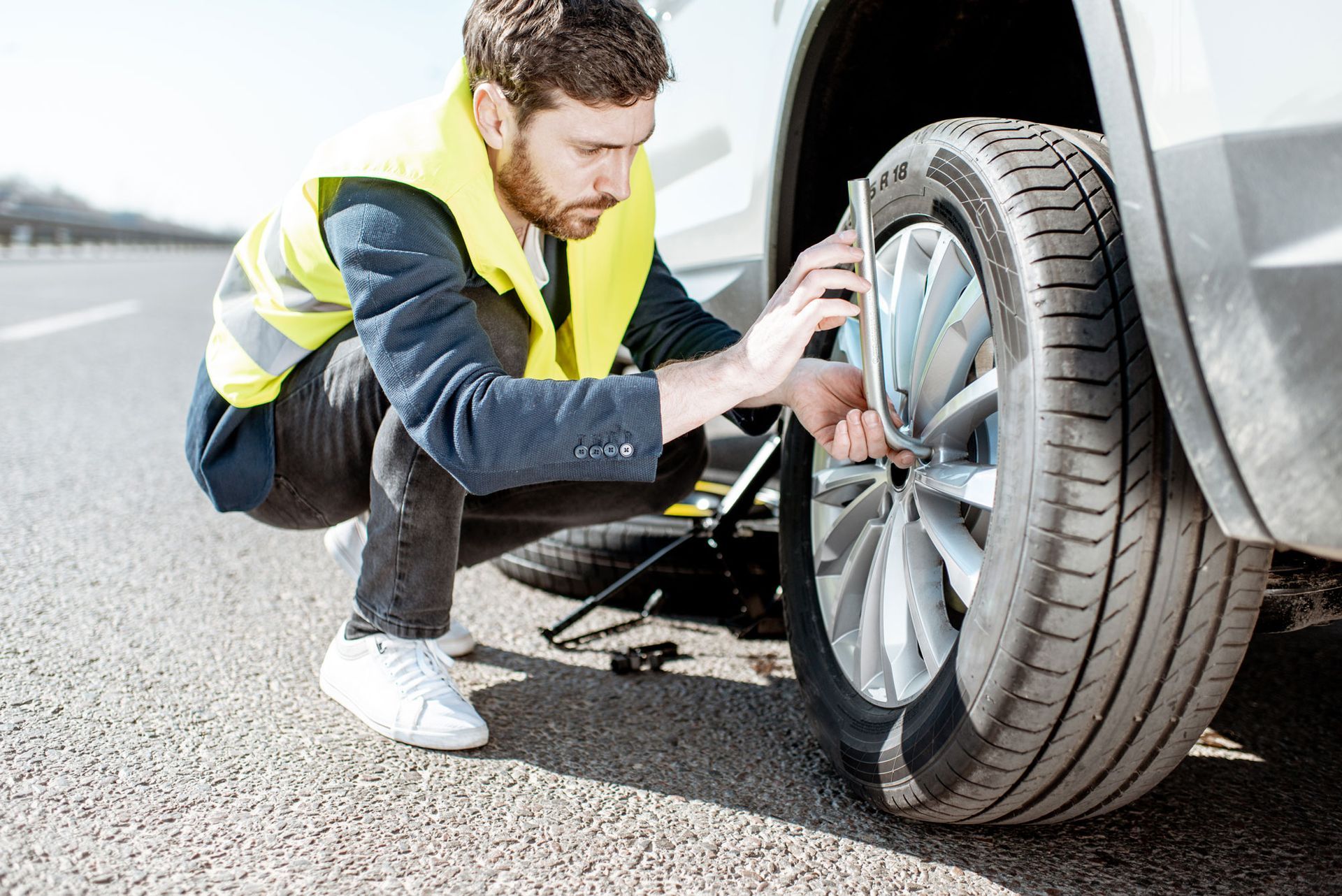 Man in yellow vest changes a flat tire on a road.