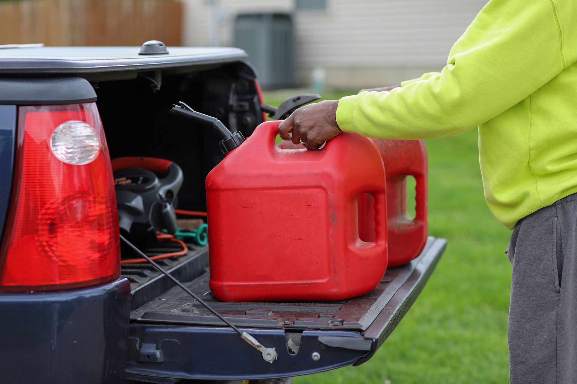 Person in a yellow jacket handling a red gas can in a pickup truck bed.