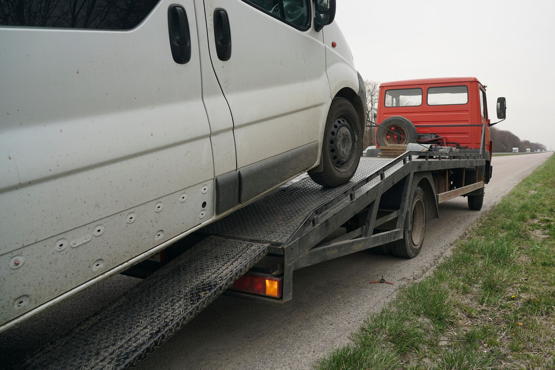 A tow truck is carrying a white van on a roadside.