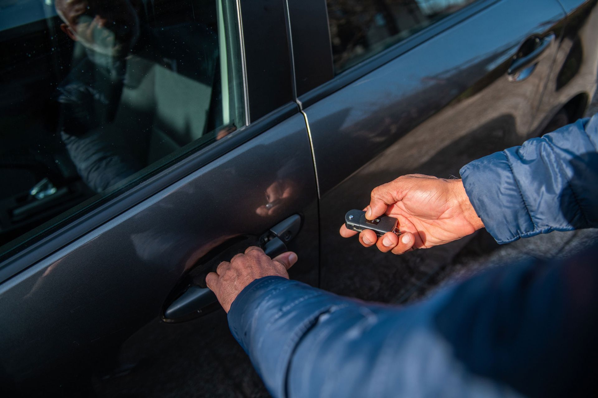 Person unlocking and opening a car door with a key fob on a sunny day.