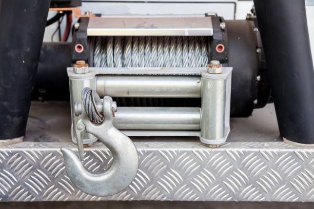 A heavy-duty winch attached to a vehicle bumper with a large hook and steel cable.