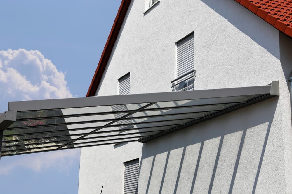 A Modern White House With a Red Roof Features a Sleek Glass Awning Casting Distinct Shadows