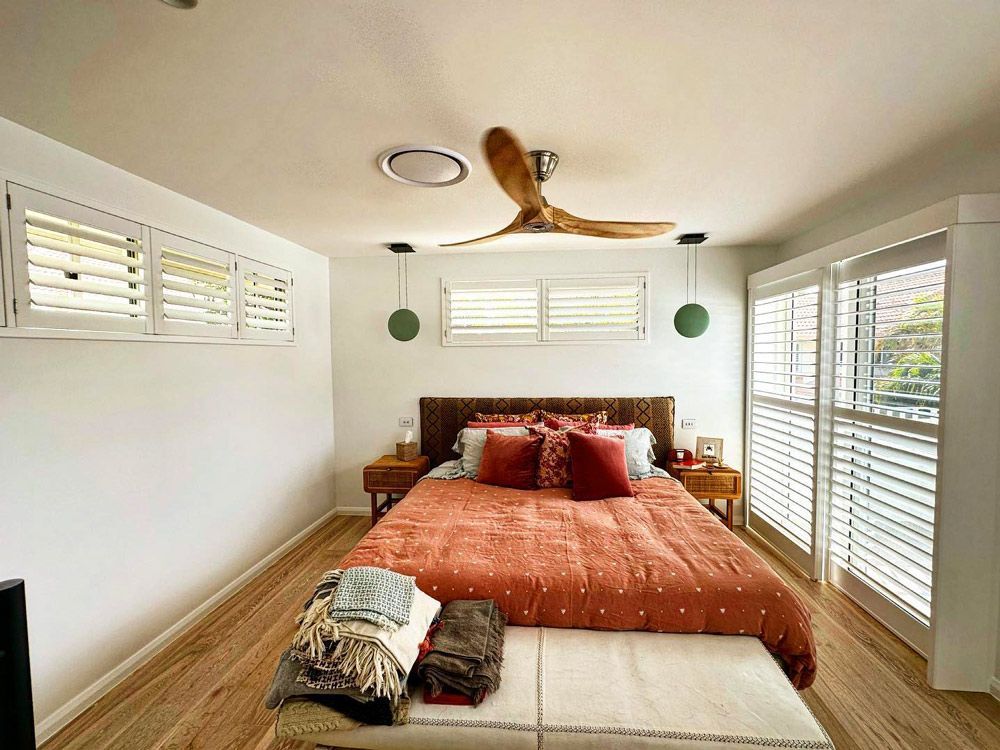 A Bedroom With a Bed, Ceiling Fan, and Shutters — TT Shutters & Shading In Ballina, NSW