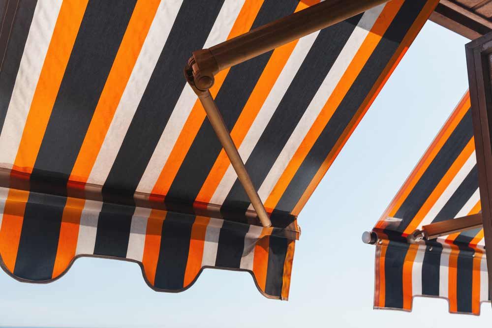 A Black and Orange Striped Awning on a Building — TT Shutters & Shading In Ballina, NSW