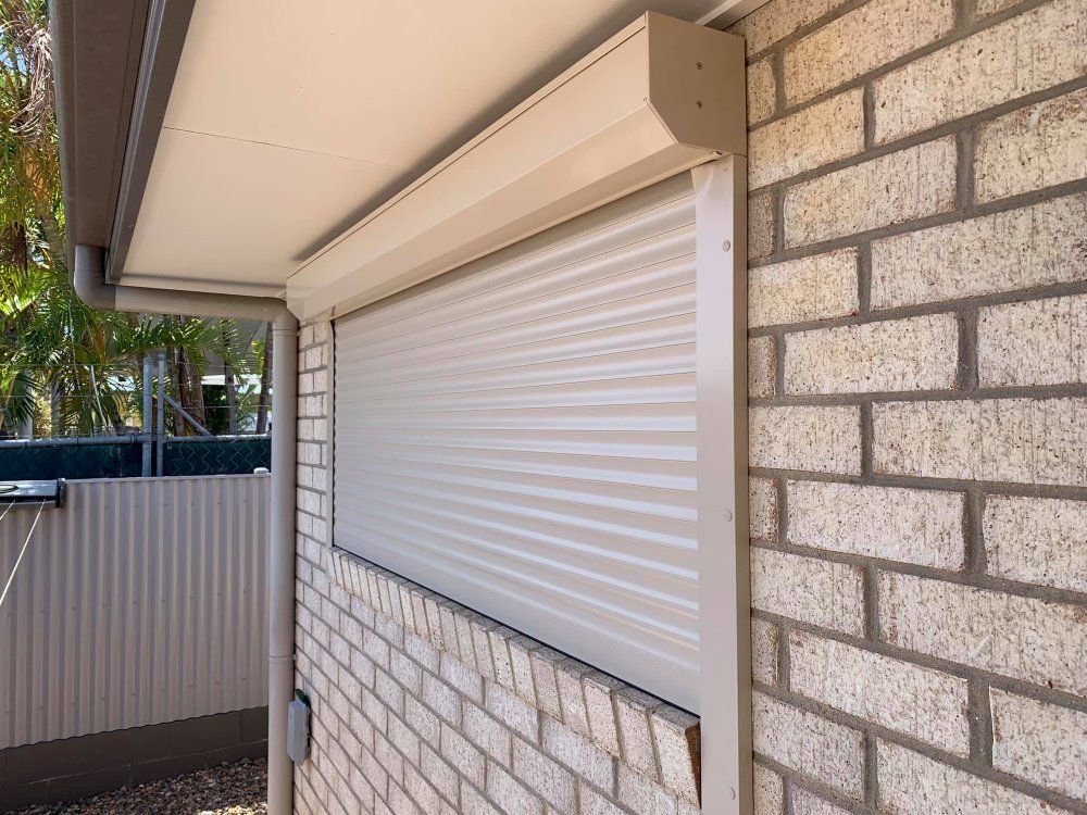 A Brick Building With A White Roller Shutter On The Window — TT Shutters & Shading In Ballina, NSW