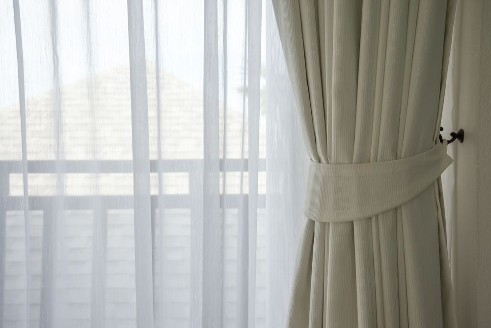 Cream-colored Draped Curtain Tied Back, Sheer White Curtain Behind, Window With Railing Visible — TT Shutters & Shading In Ballina, NSW