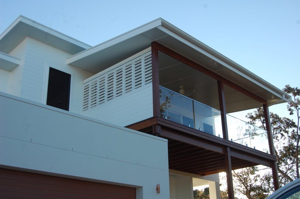 A White House With a Balcony and a Car Parked in Front of It — TT Shutters & Shading In Ballina, NSW