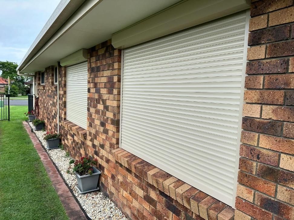 A Brick House With White Roller Shutters on the Windows — TT Shutters & Shading In Ballina, NSW