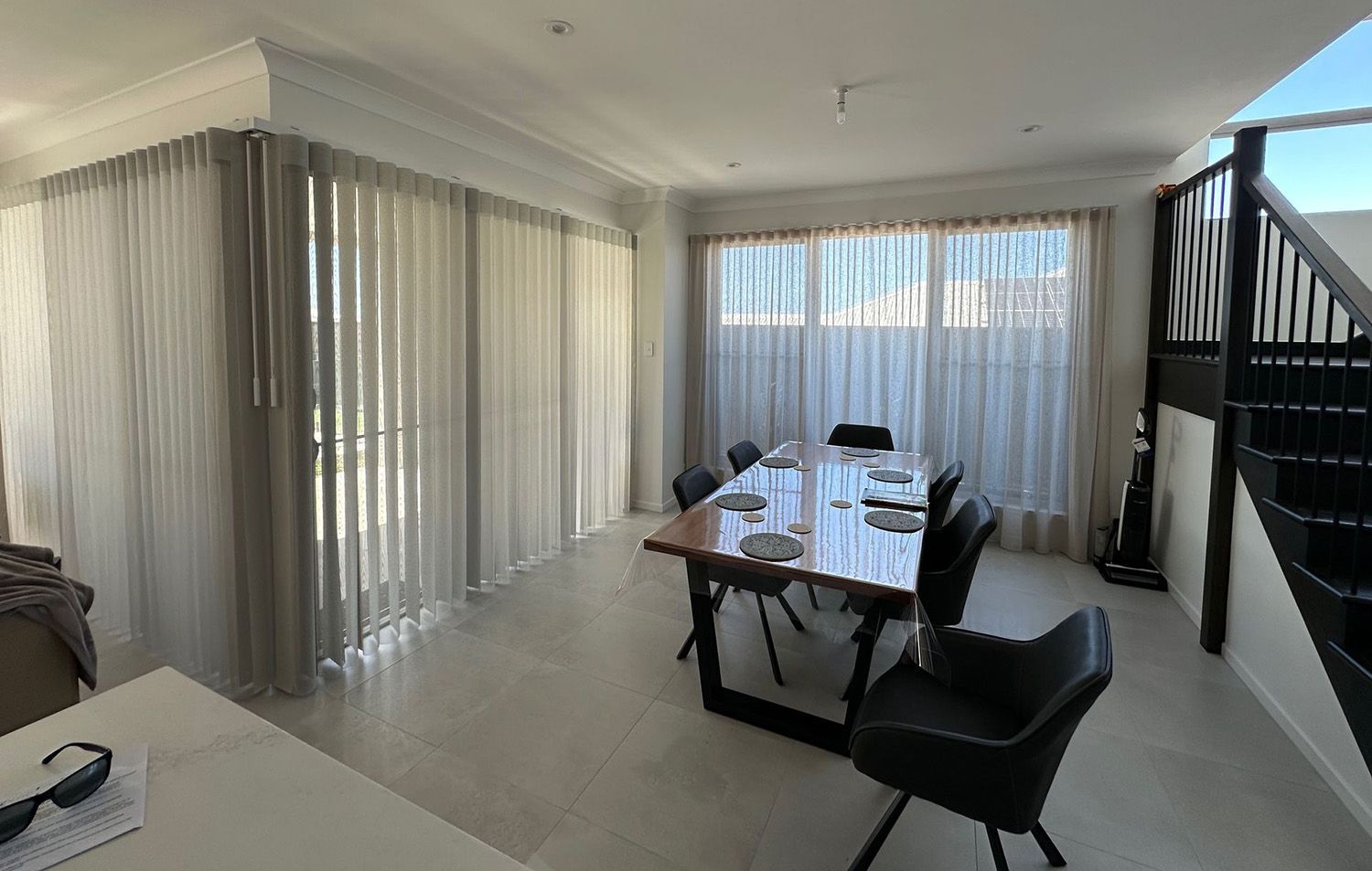 A Dining Area With Floor-To-Ceiling White Sheer Curtains, Next To A Black Staircase