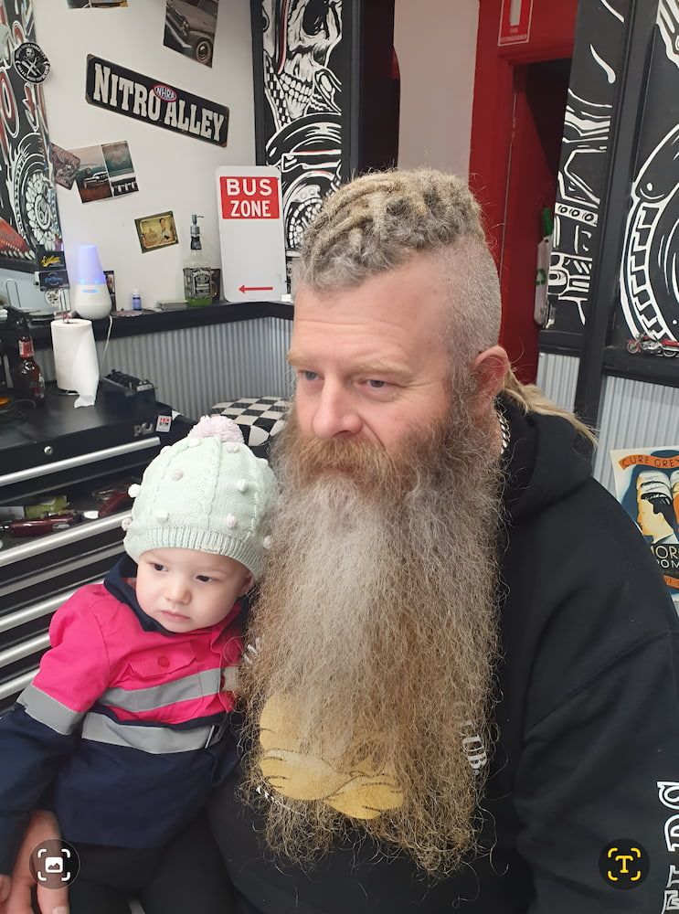 A Man With A Beard Is Holding A Baby In His Arms — Get It Off Men's Barber Shop In Raymond Terrace, NSW