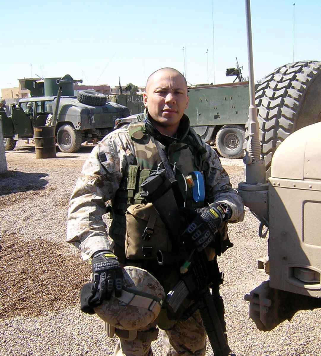 Anthony Guzman, in a navy uniform, stands in front of military vehicles.