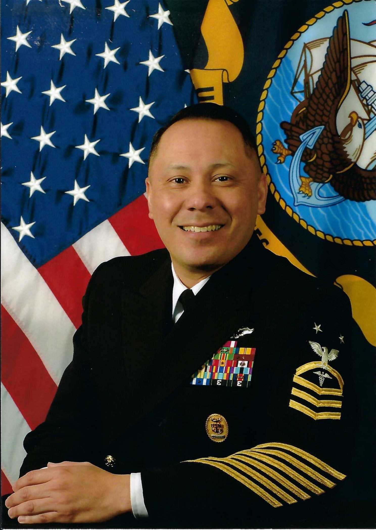 Anthony Guzman, in a navy uniform, stands in front of the American flag