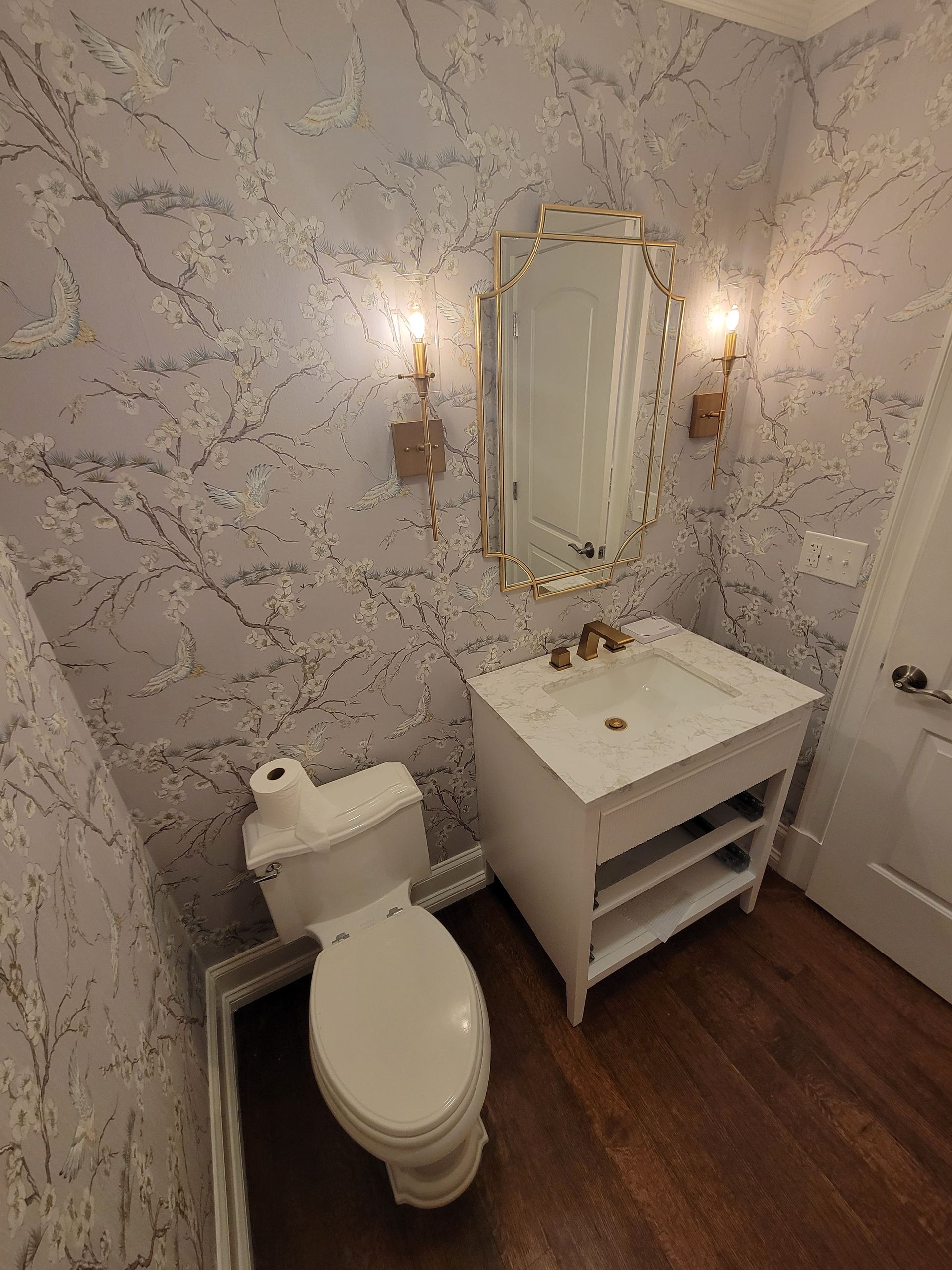 Small bathroom with a toilet, sink, mirror, and patterned wallpaper.
