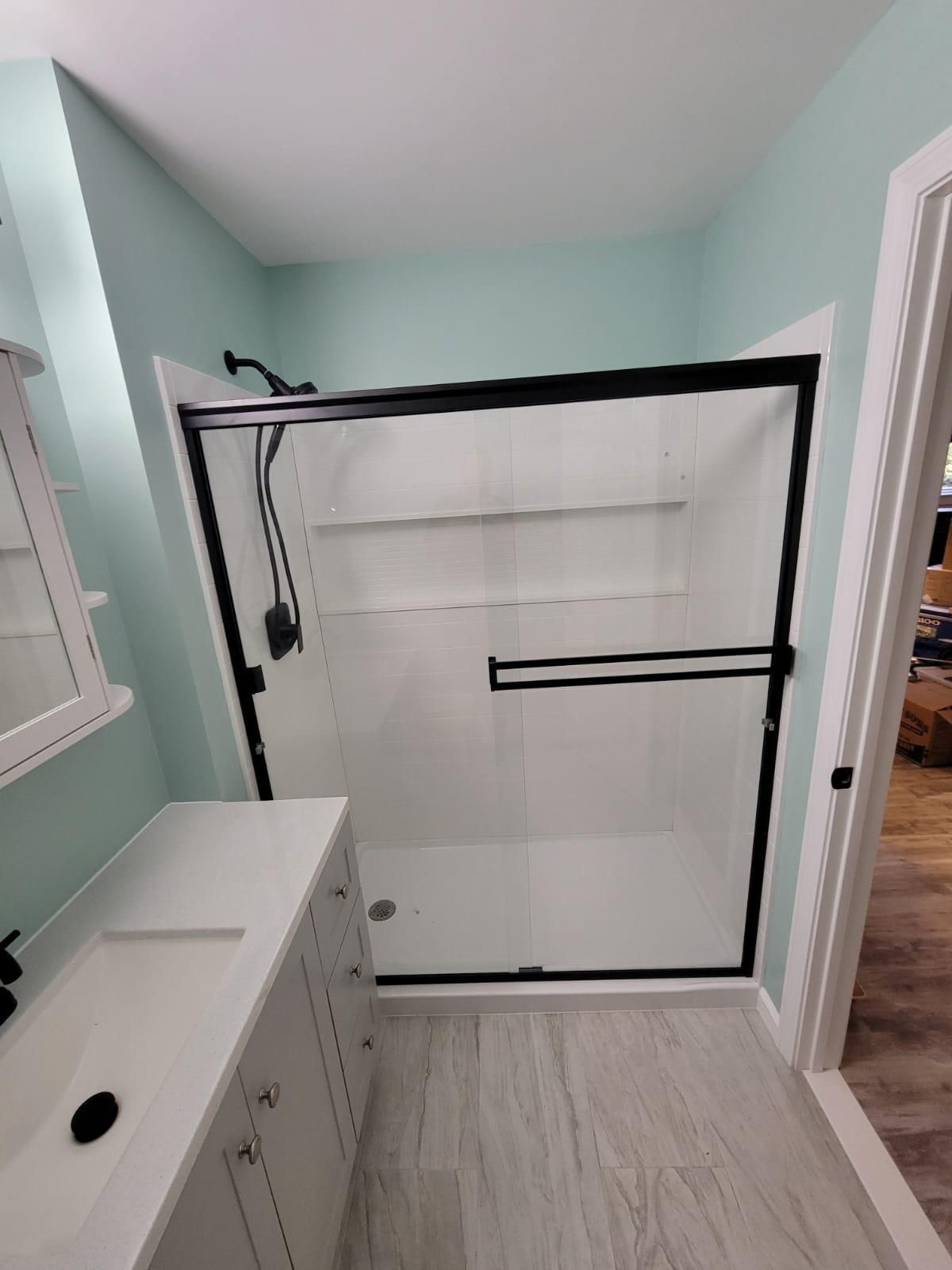 Bathroom with white shower enclosure, black frame, mint walls, white vanity, and gray tile floor.