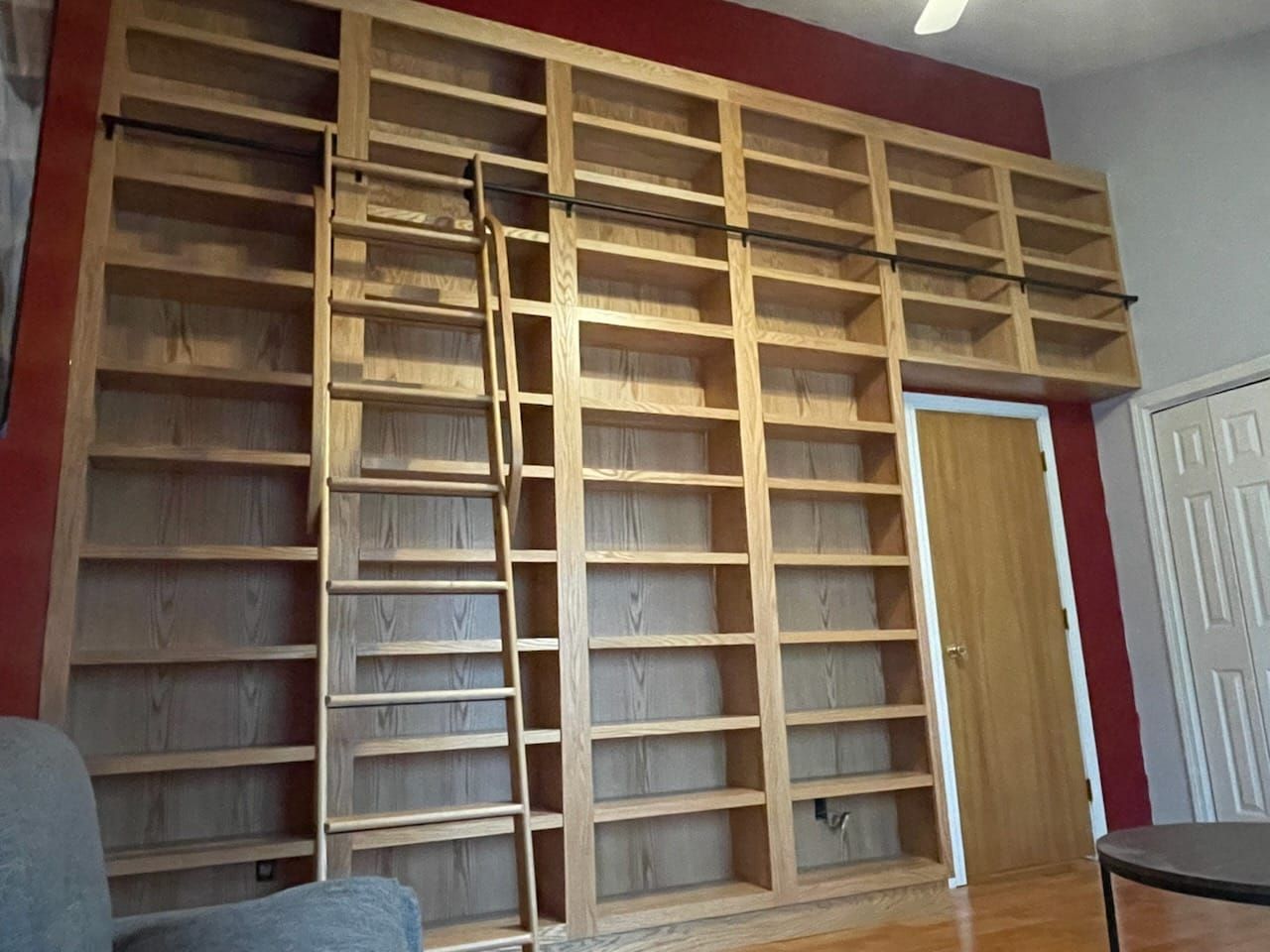 Large wooden bookshelf with ladder against a red wall, next to a door.