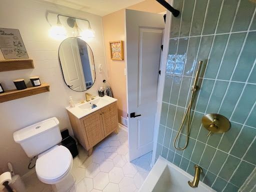 Bathroom with green tiled shower, white toilet, wooden vanity, and oval mirror.
