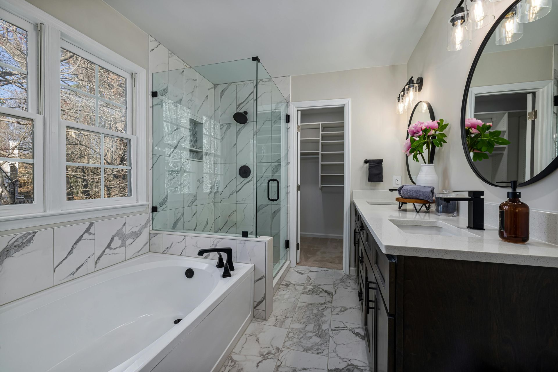 Modern bathroom with white marble tile, glass shower, and dark vanity.